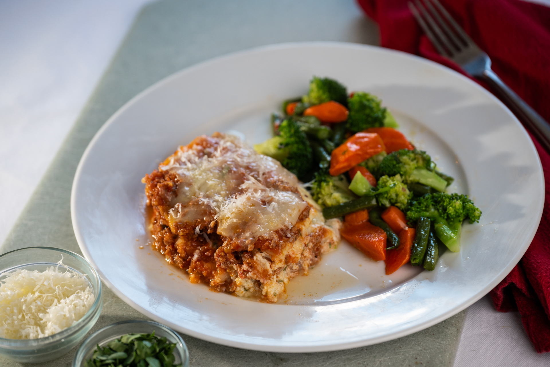 A slice of scratch-made lasagna with sautéed vegetables and parmesan