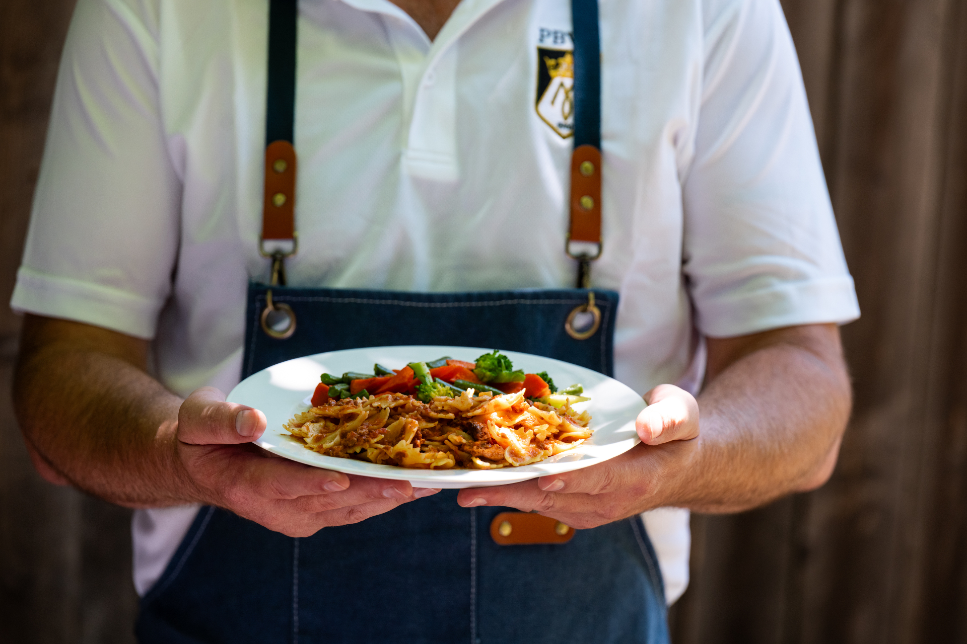 Hands holding a plate of scratch-made pasta with sauteed vegetables